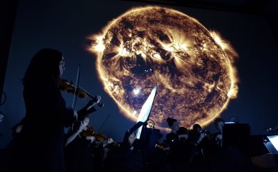 An orchestra playing against a NASA image of a celestial object for Space Music