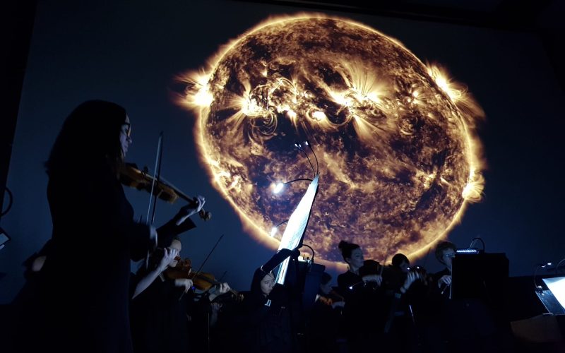 An orchestra playing against a NASA image of a celestial object for Space Music